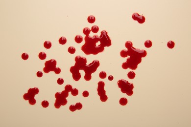 Drops of blood on beige background, top view