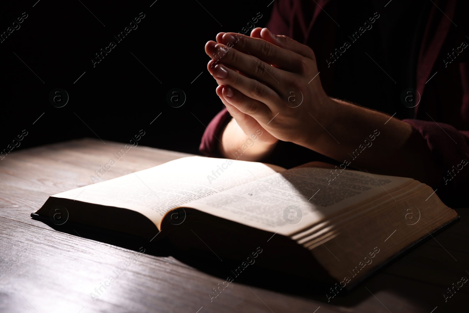 Photo of Man with Bible praying at wooden table, closeup