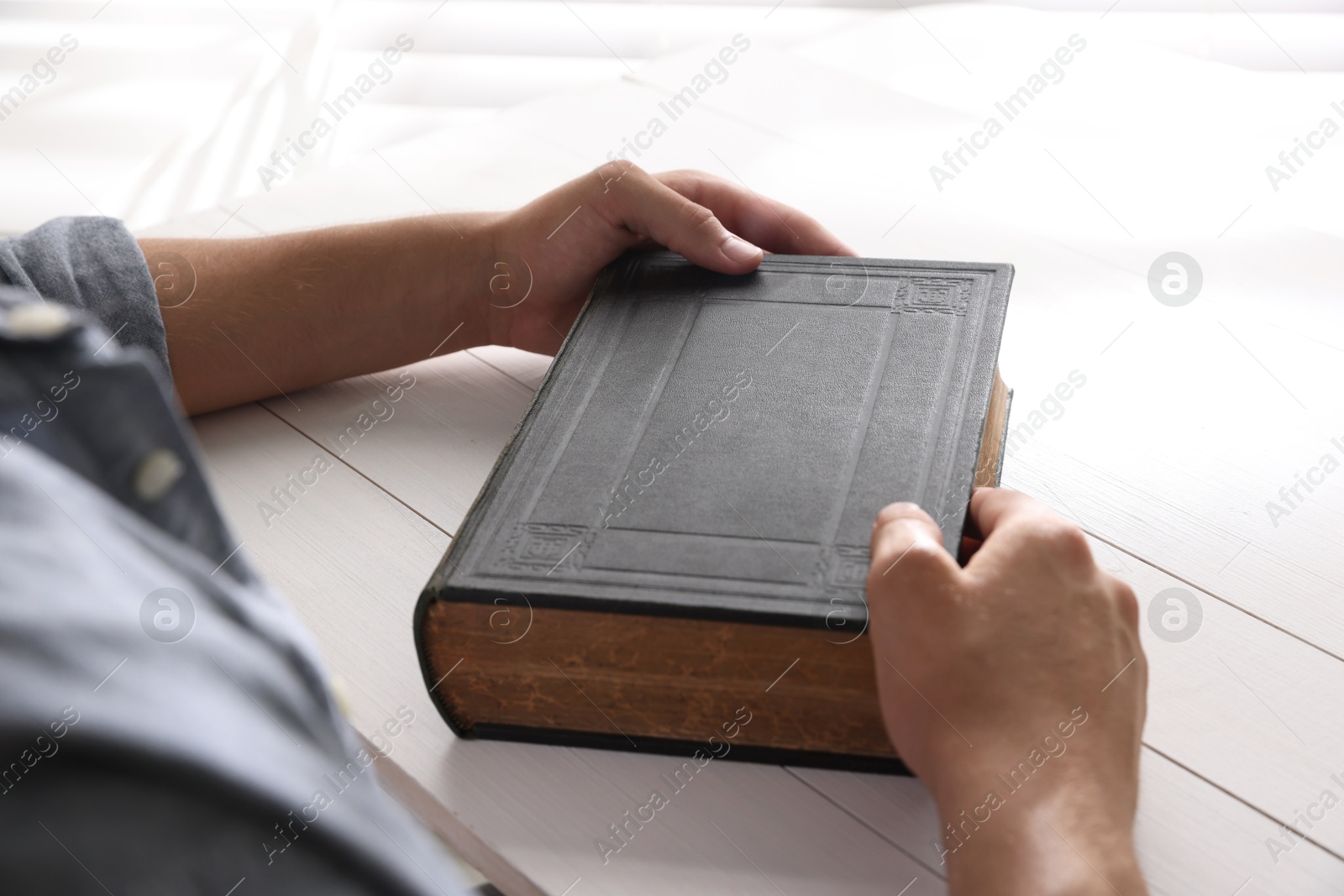 Photo of Man with Bible at white wooden table, closeup