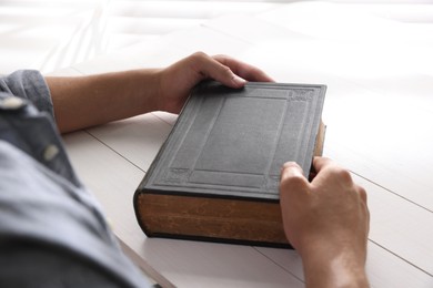 Photo of Man with Bible at white wooden table, closeup