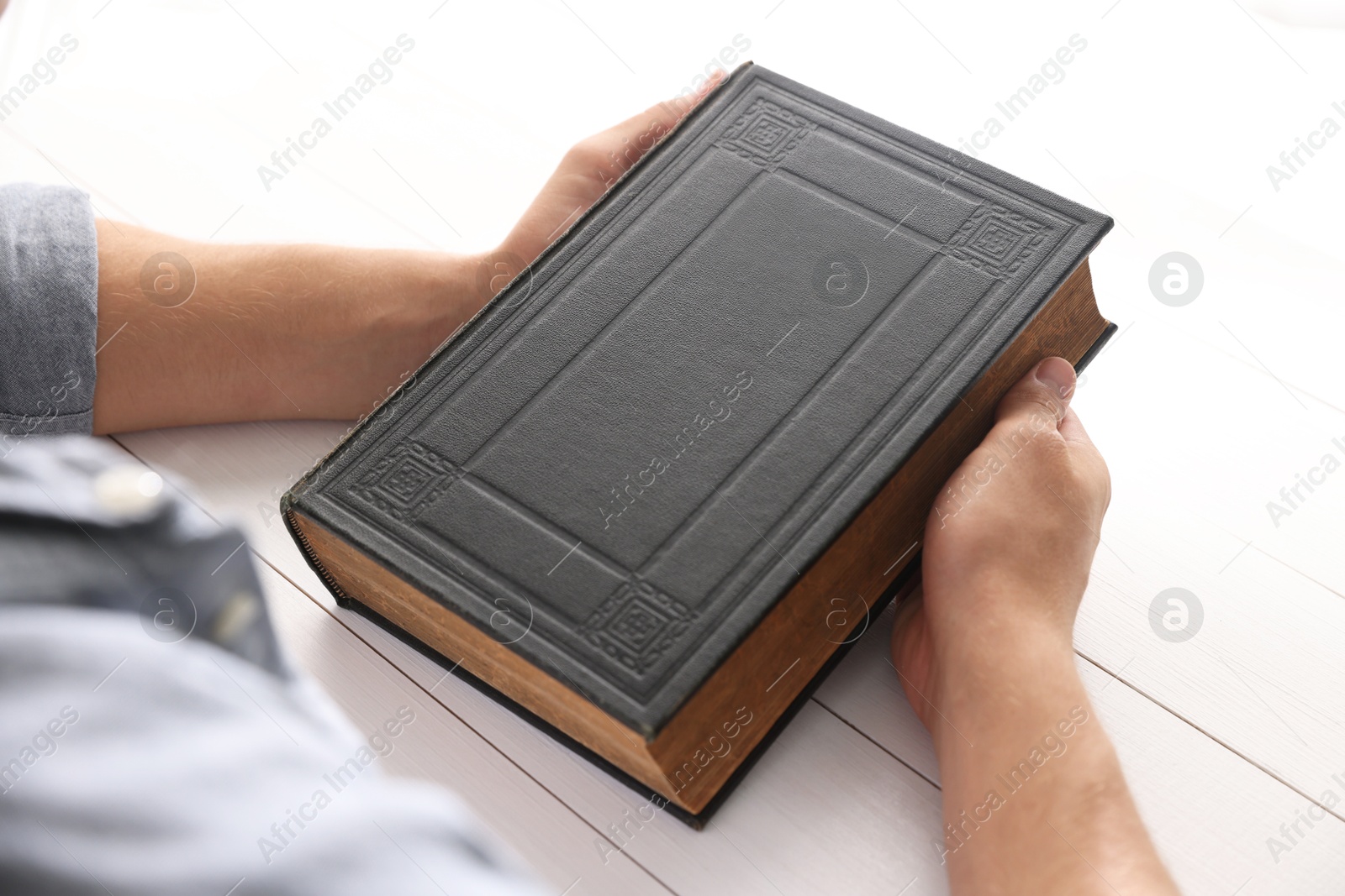 Photo of Man with Bible at white wooden table, closeup