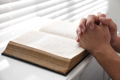 Photo of Man with Bible praying at white table, closeup