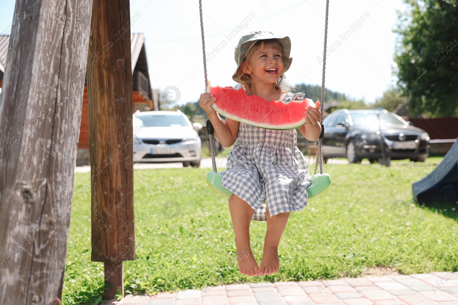 Photo of Cute little girl with slice of juicy watermelon on swing outdoors