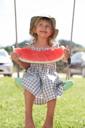 Cute little girl with slice of juicy watermelon on swing outdoors