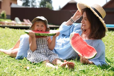 Photo of Mother and her daughter eating juicy watermelon on green grass outdoors