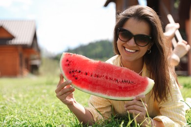 Photo of Happy woman holding slice of juicy watermelon on green grass outdoors