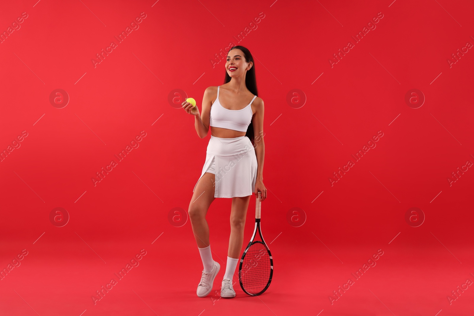 Photo of Beautiful young woman with tennis racket and ball on red background