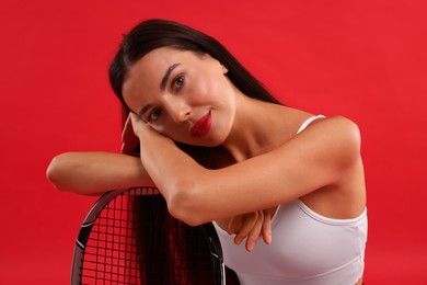 Beautiful young woman with tennis racket on red background