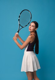 Beautiful young woman with tennis racket on light blue background