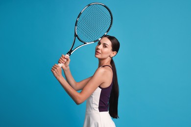 Beautiful young woman with tennis racket on light blue background