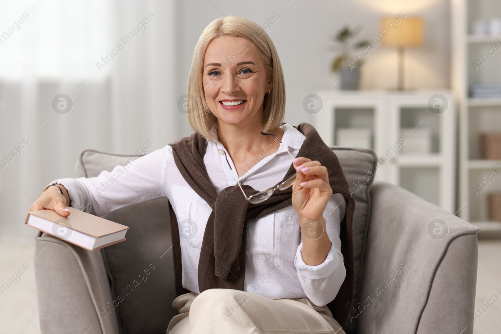 Photo of Portrait of smiling middle aged woman with glasses and book at home