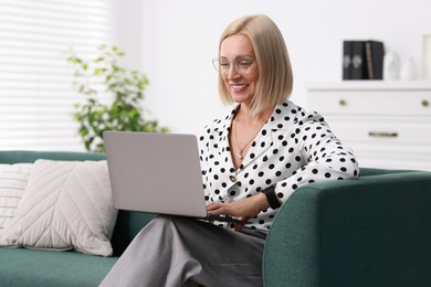 Smiling middle aged woman working with laptop on sofa at home