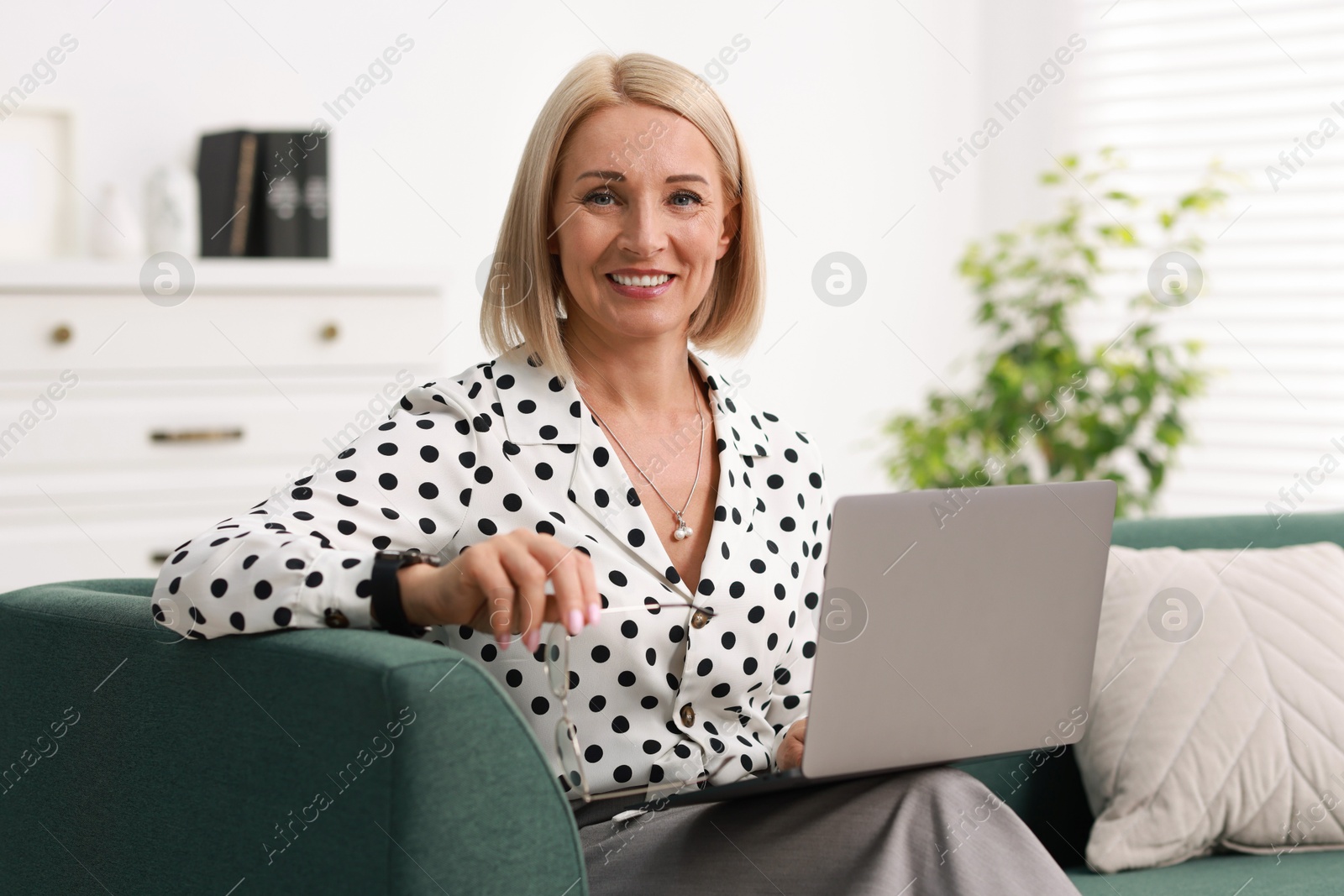 Photo of Smiling middle aged woman working with laptop on sofa at home