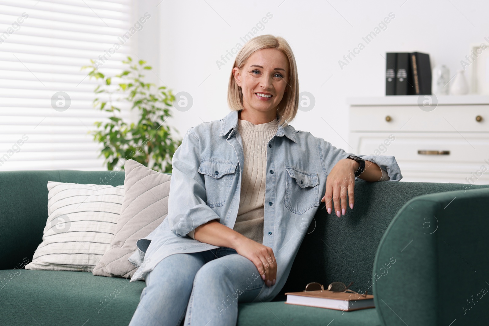 Photo of Portrait of smiling middle aged woman with book on sofa at home