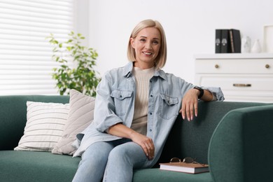 Photo of Portrait of smiling middle aged woman with book on sofa at home