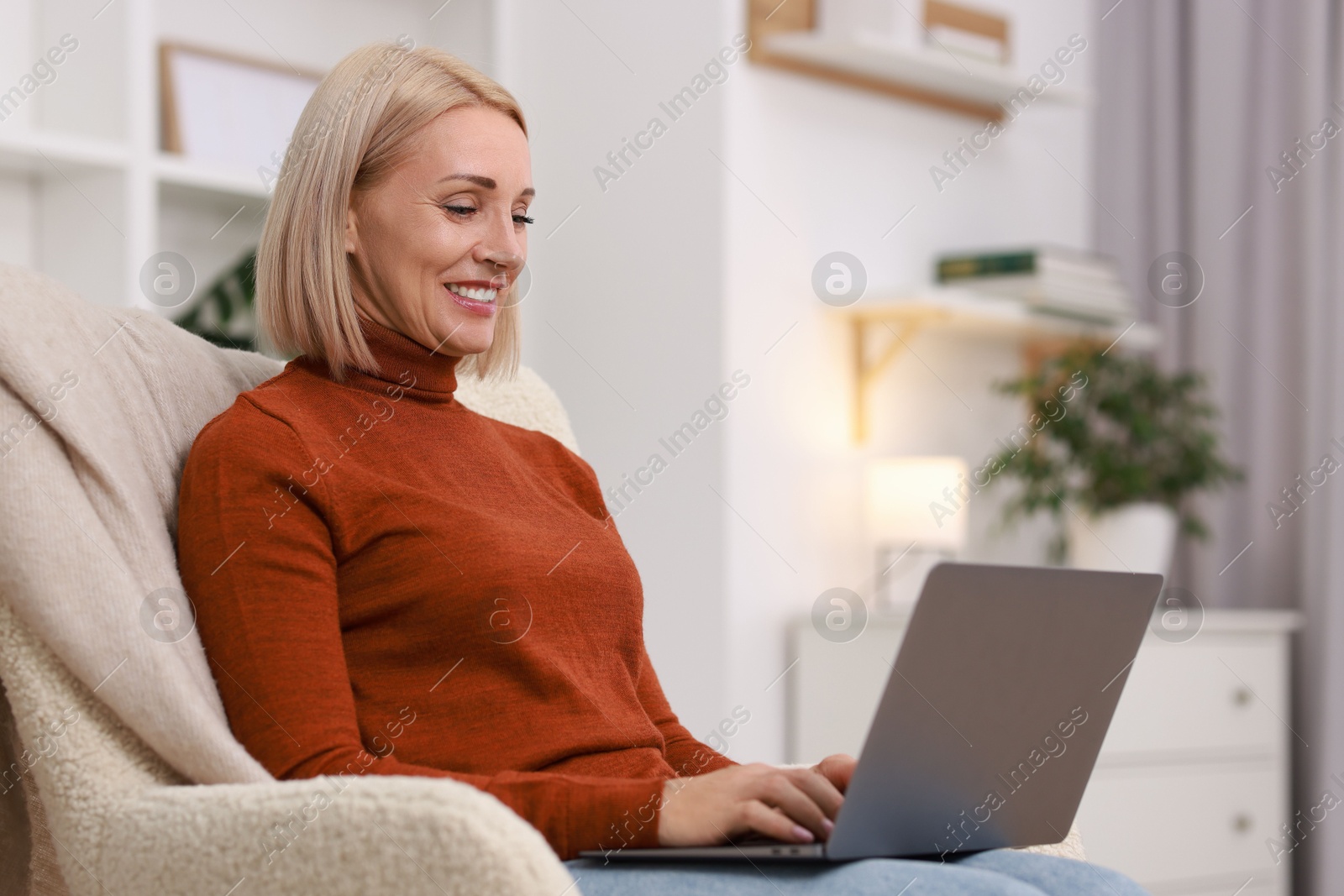 Photo of Portrait of smiling middle aged woman with laptop on armchair at home