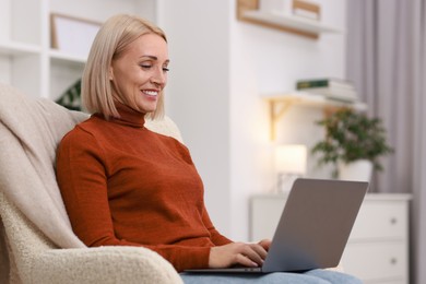 Photo of Portrait of smiling middle aged woman with laptop on armchair at home