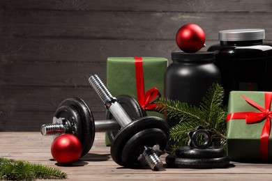 Photo of Dumbbells, containers with supplement and Christmas decor on wooden table