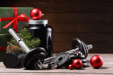 Photo of Dumbbells, container with supplement and Christmas decor on wooden table