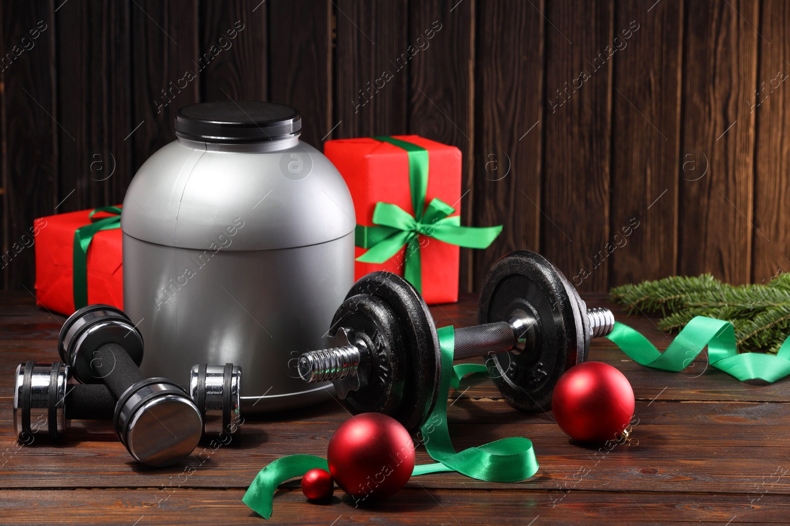 Photo of Dumbbells, container with supplement and Christmas decor on wooden table