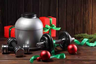 Photo of Dumbbells, container with supplement and Christmas decor on wooden table