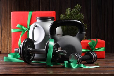 Photo of Dumbbells, container with supplement, kettlebell and Christmas decor on wooden table