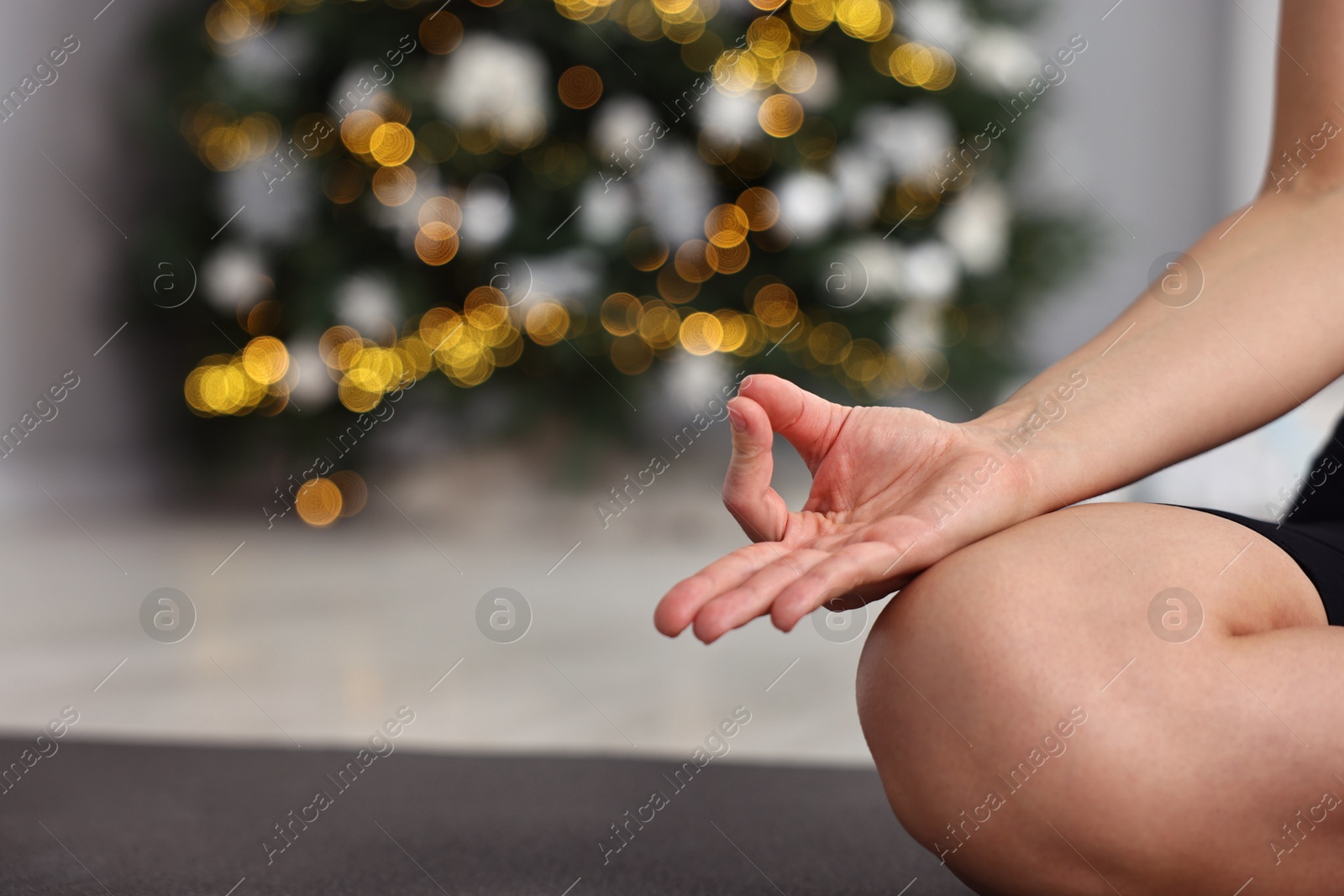 Photo of Woman practicing yoga against blurred Christmas lights indoors, closeup