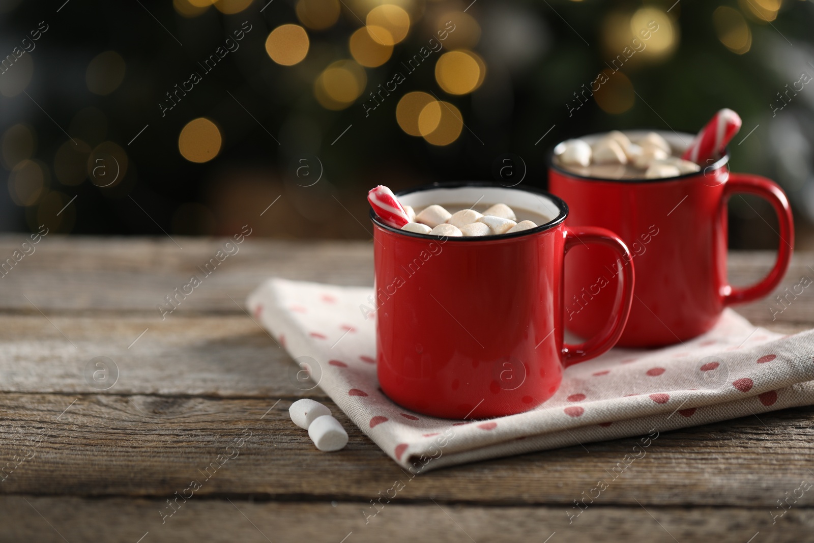 Photo of Tasty hot cocoa drink with candy canes and marshmallows in red mugs on wooden table, space for text