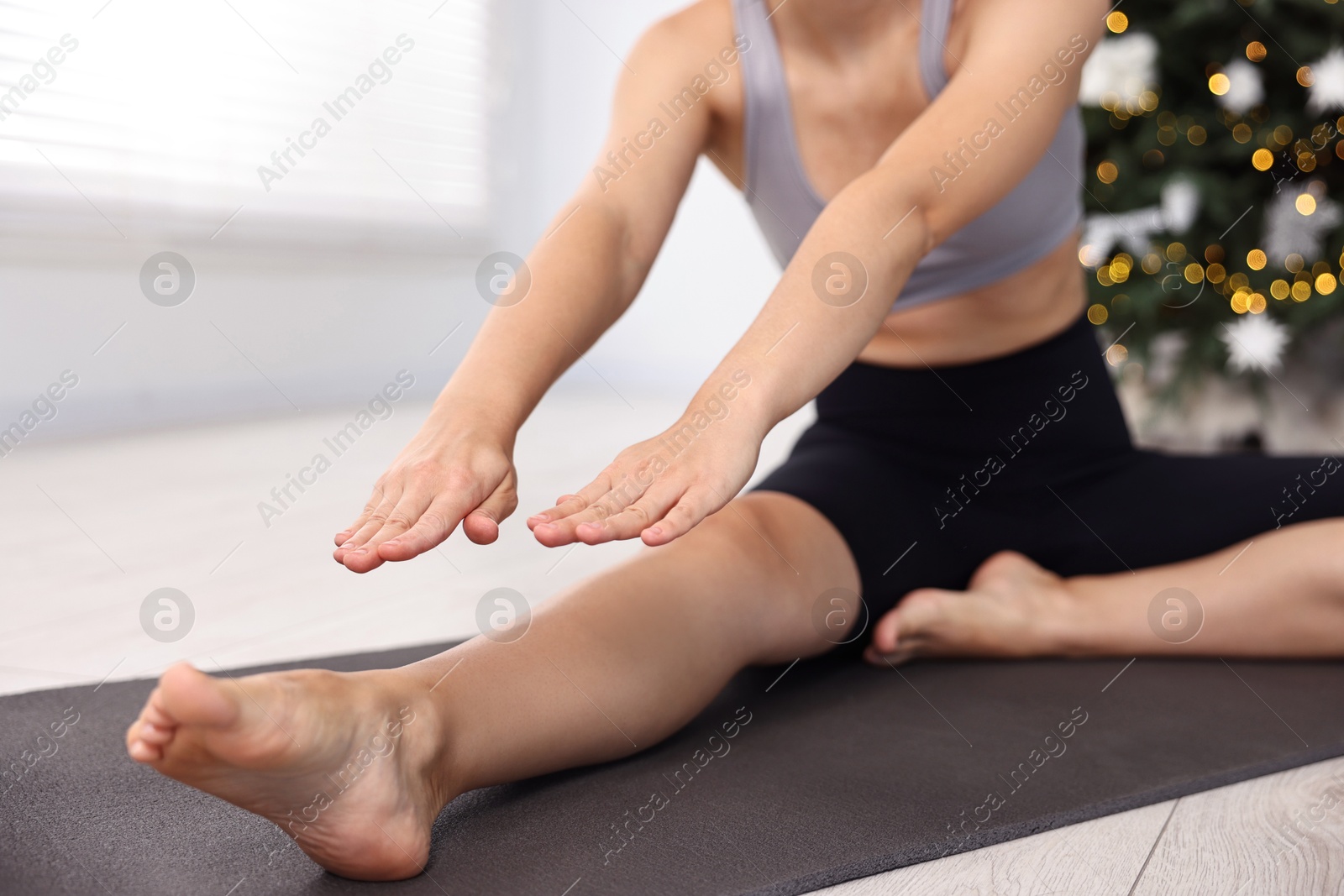 Photo of Woman practicing yoga against blurred Christmas lights indoors, closeup