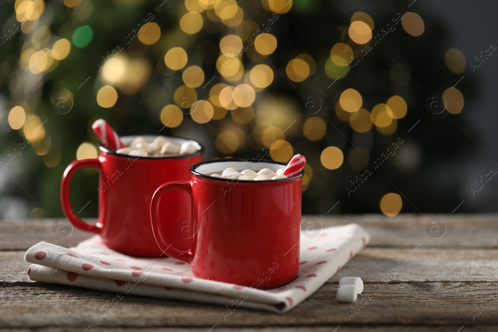 Photo of Tasty hot cocoa drink with candy canes and marshmallows in red mugs on wooden table