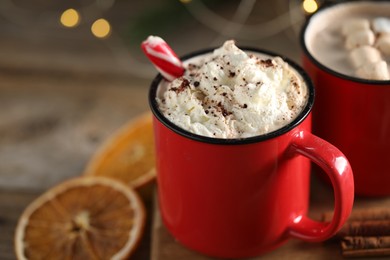 Photo of Tasty hot cocoa drink with candy cane and whipped cream in red mugs on table, closeup