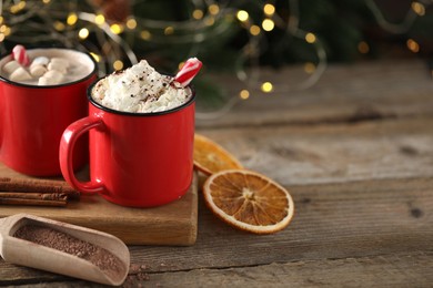 Photo of Tasty hot cocoa drink with whipped cream in mugs and dry orange on wooden table, space for text