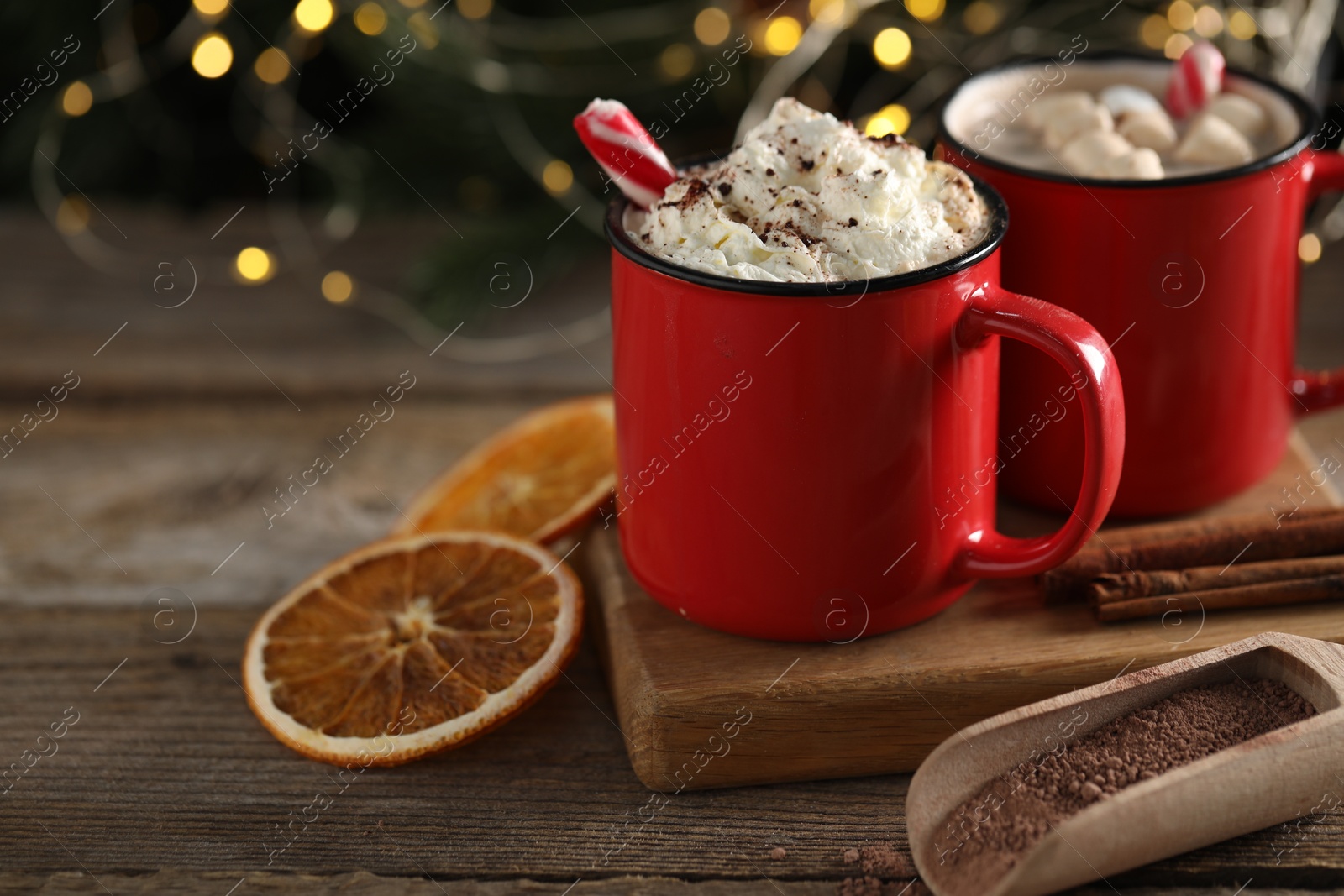 Photo of Tasty hot cocoa drink with whipped cream in red mugs and dry orange on wooden table