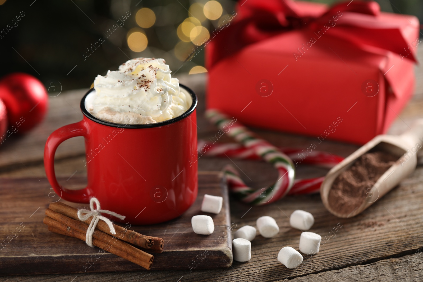 Photo of Tasty hot cocoa drink with whipped cream in mug, marshmallows and spices on wooden table