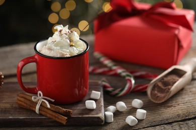 Photo of Tasty hot cocoa drink with whipped cream in mug, marshmallows and spices on wooden table