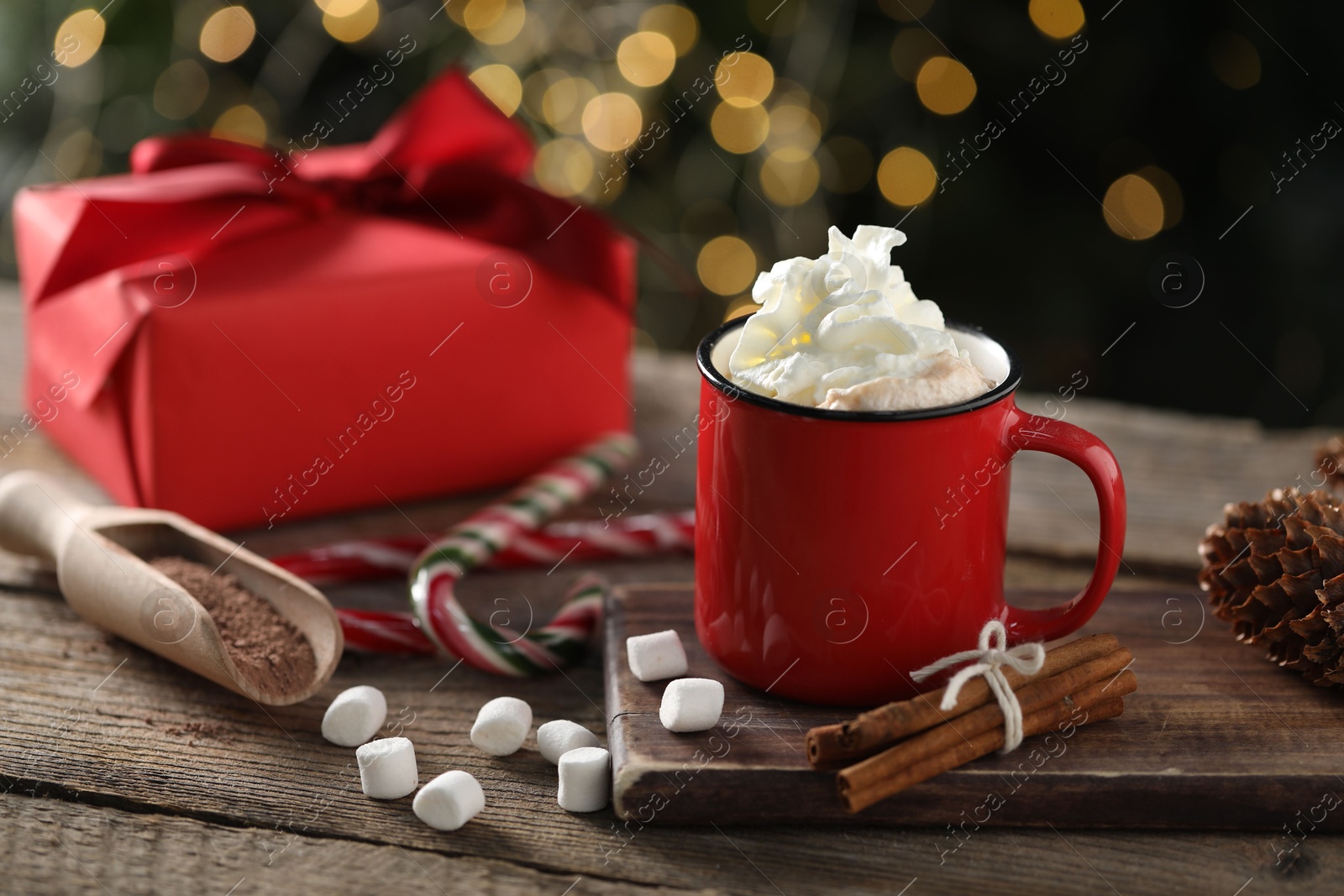 Photo of Tasty hot cocoa drink with whipped cream in mug, marshmallows and spices on wooden table