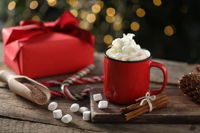 Photo of Tasty hot cocoa drink with whipped cream in mug, marshmallows and spices on wooden table