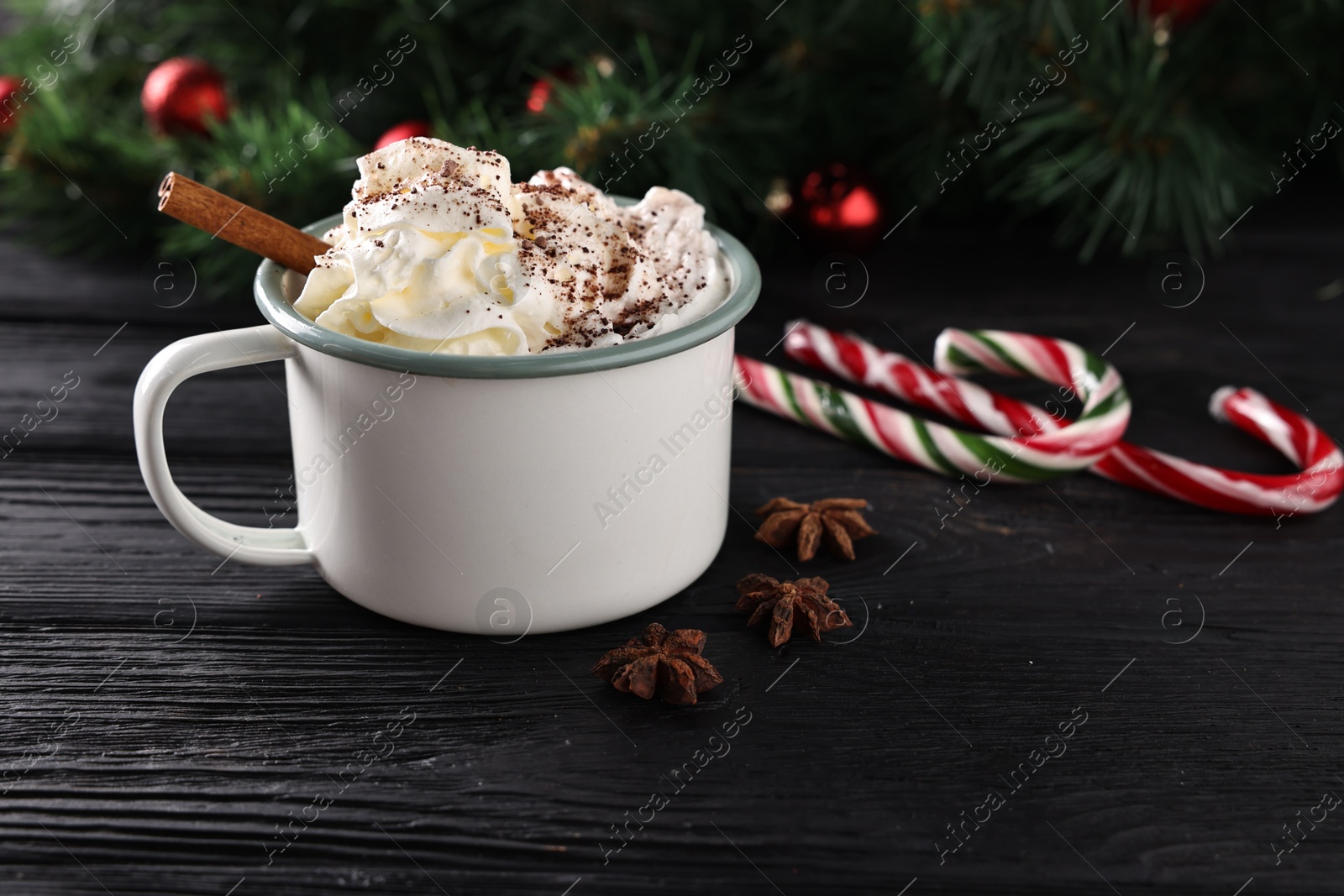 Photo of Tasty hot cocoa drink with whipped cream in mug and spices on black wooden table