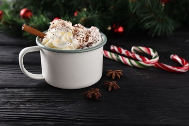 Photo of Tasty hot cocoa drink with whipped cream in mug and spices on black wooden table