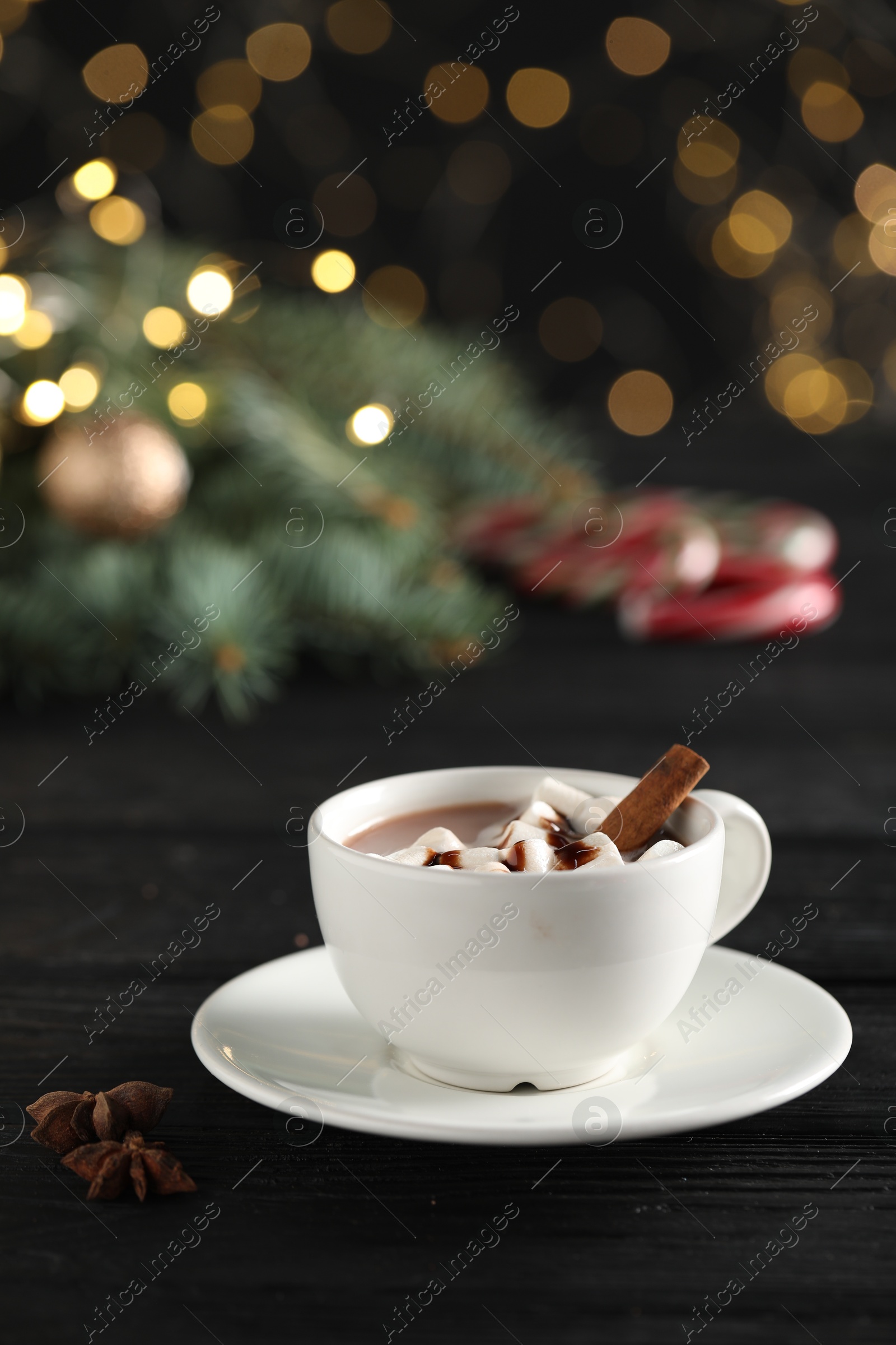 Photo of Tasty hot cocoa drink with marshmallows in cup and spices on black wooden table