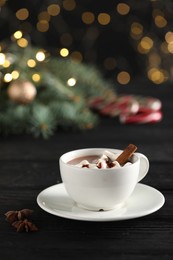 Photo of Tasty hot cocoa drink with marshmallows in cup and spices on black wooden table