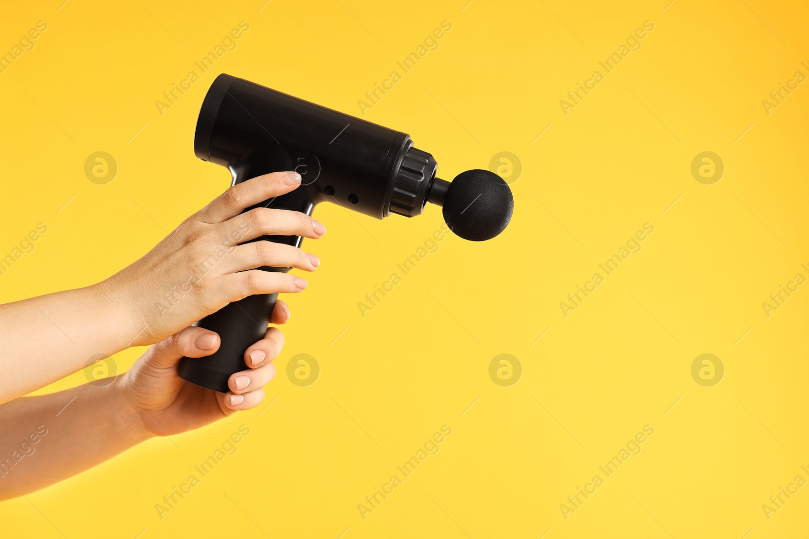 Photo of Woman holding percussive massager on yellow background, closeup. Space for text