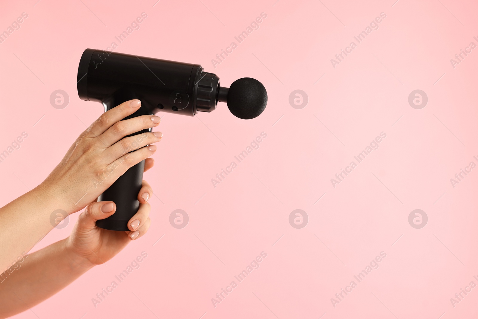 Photo of Woman holding percussive massager on pink background, closeup. Space for text