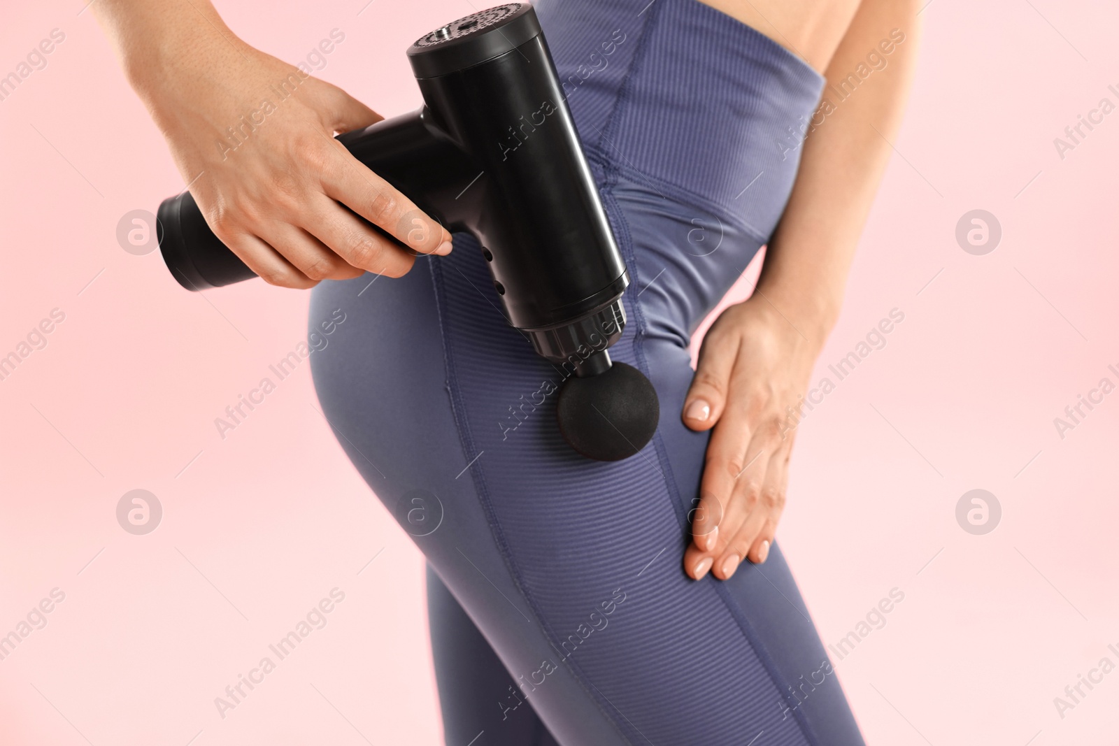 Photo of Woman using percussive massager to relax hip muscles on pink background, closeup