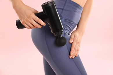 Woman using percussive massager to relax hip muscles on pink background, closeup