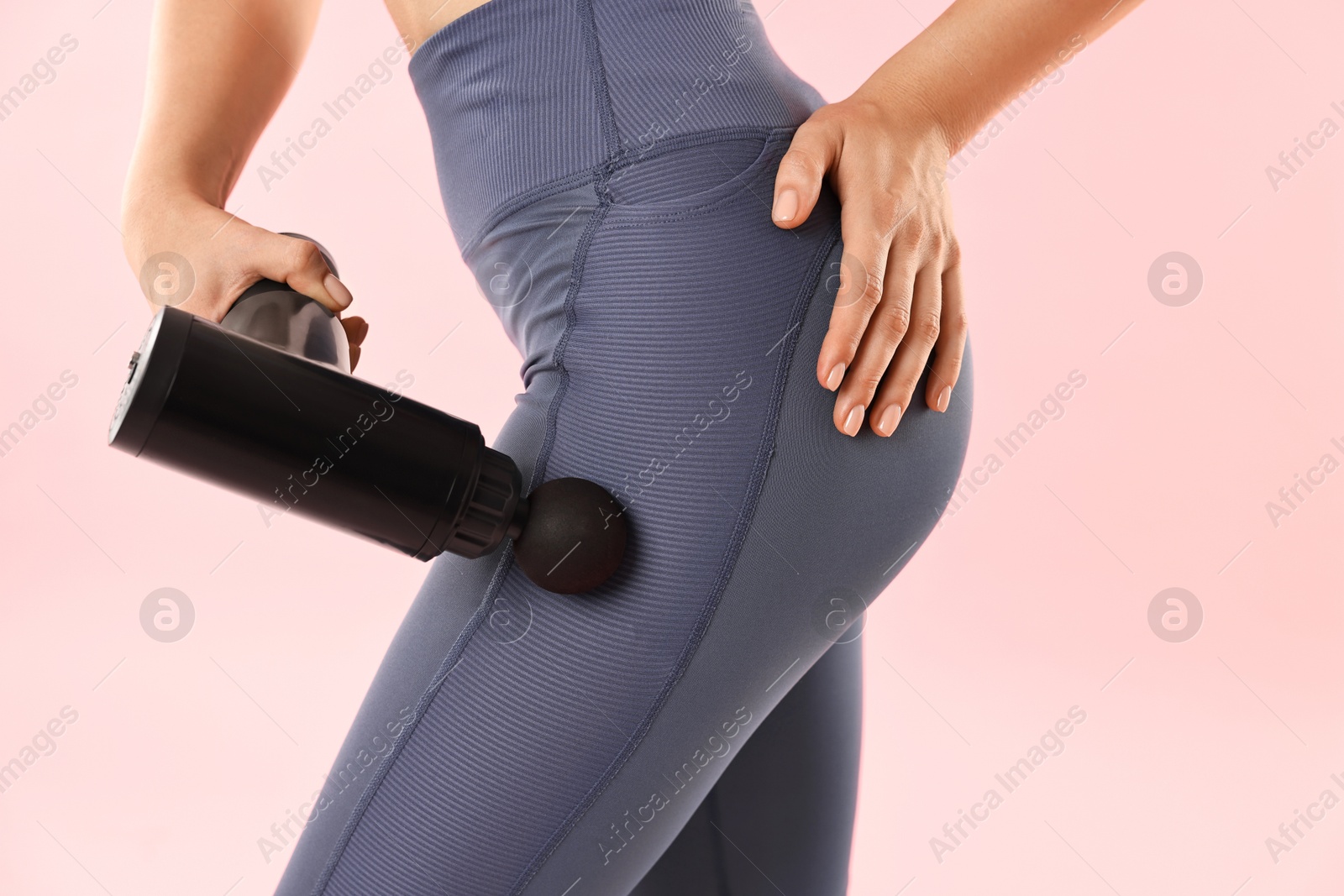 Photo of Woman using percussive massager to relax hip muscles on pink background, closeup