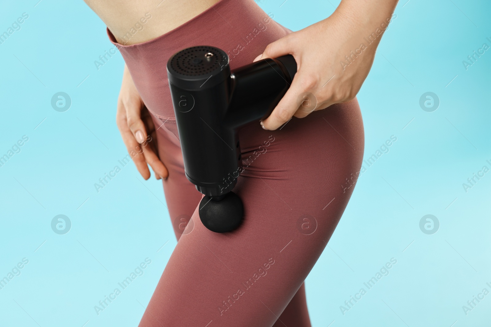 Photo of Woman using percussive massager to relax hip muscles on light blue background, closeup