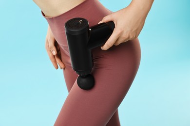 Woman using percussive massager to relax hip muscles on light blue background, closeup