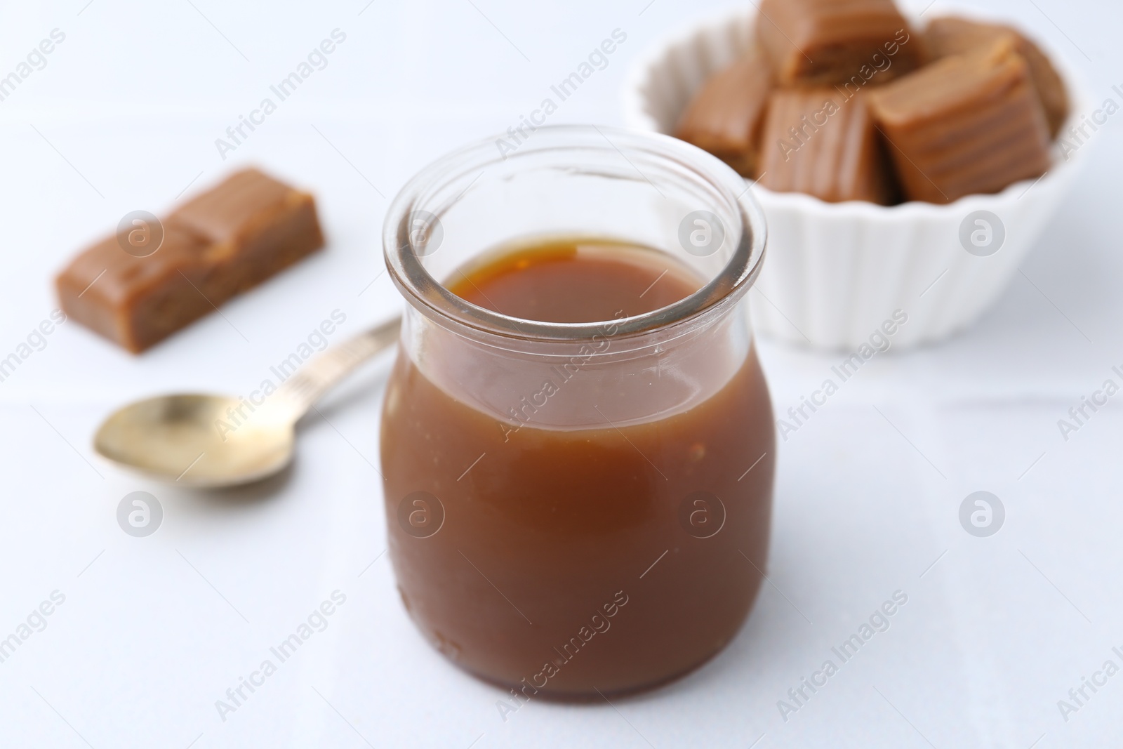 Photo of Tasty caramel sauce in jar on white table, closeup