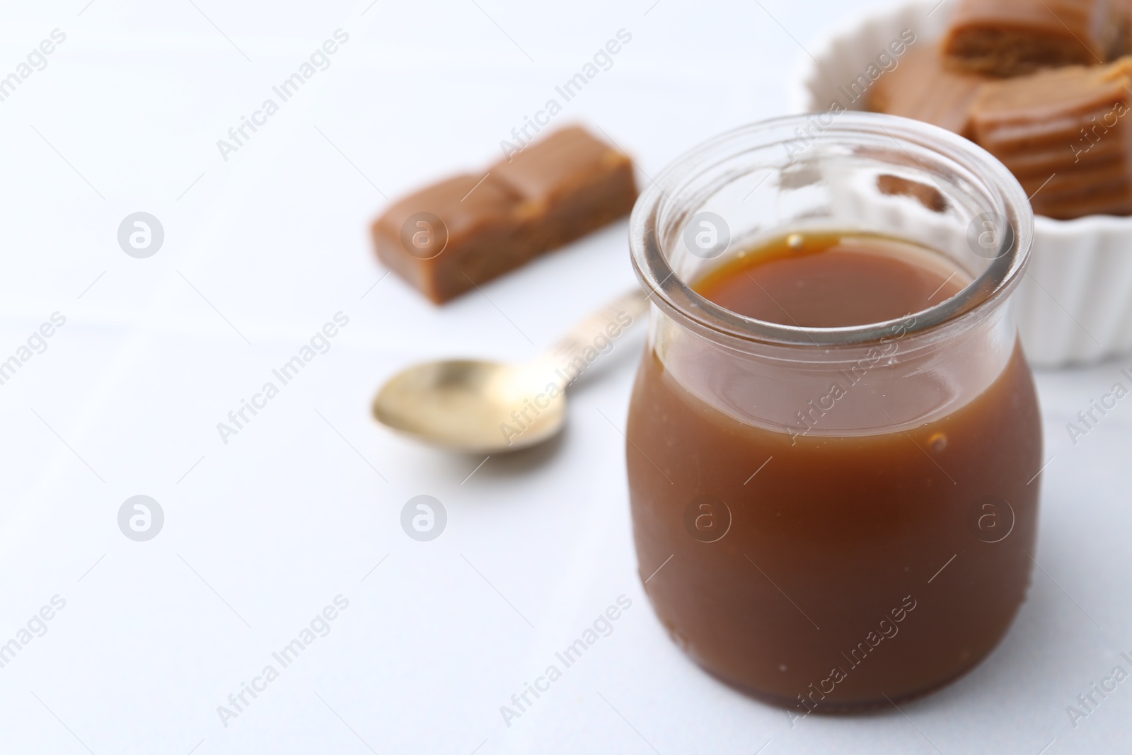 Photo of Tasty caramel sauce in jar on white table, closeup. Space for text